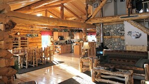 A rustic cabin interior with a wooden dining area, kitchen, and a stone wall. - Log Cabin Wilderness Lodge (Tok)