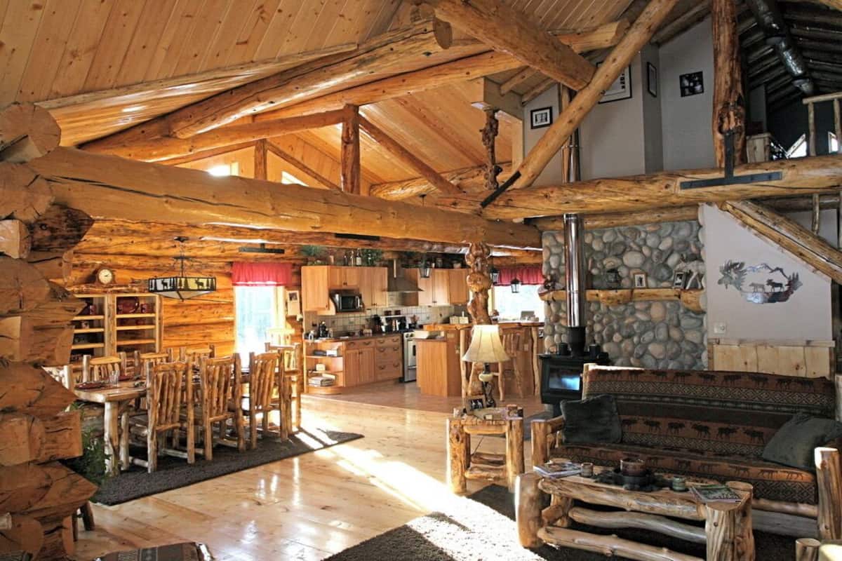 A rustic cabin interior with a wooden dining area, kitchen, and a stone wall.