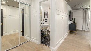 A hallway with a mirrored closet door, a white vanity with a marble countertop, and a small black and white patterned rug.