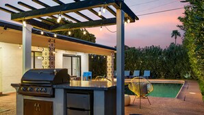 An outdoor kitchen with a grill, a refrigerator, and a covered seating area with string lights.