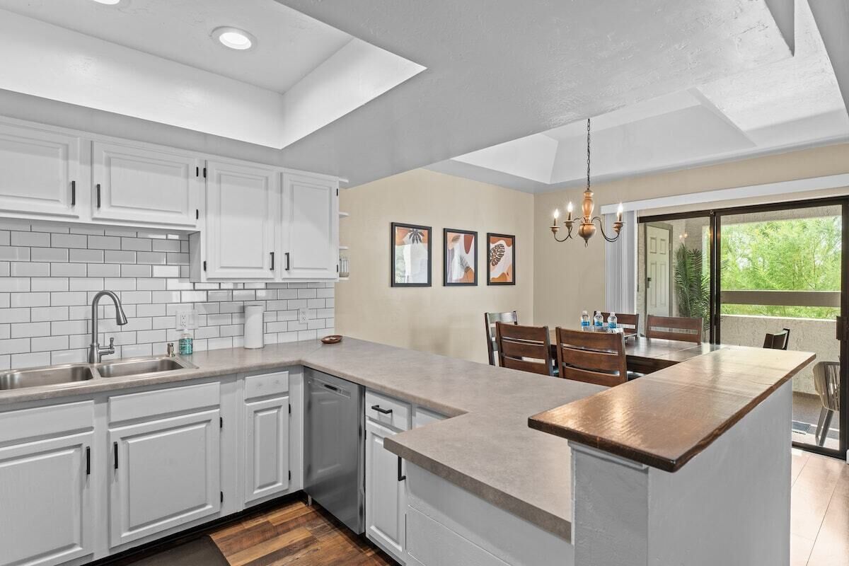 A modern kitchen with white cabinets, a large island, and a dining area with a view.