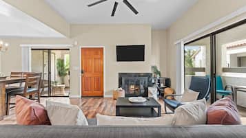 A spacious living room with a fireplace, a ceiling fan, a dining area, and a balcony with a view.