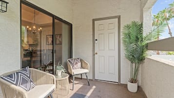 A covered patio area with wicker furniture, a potted plant, and a sliding glass door leading to an interior space.