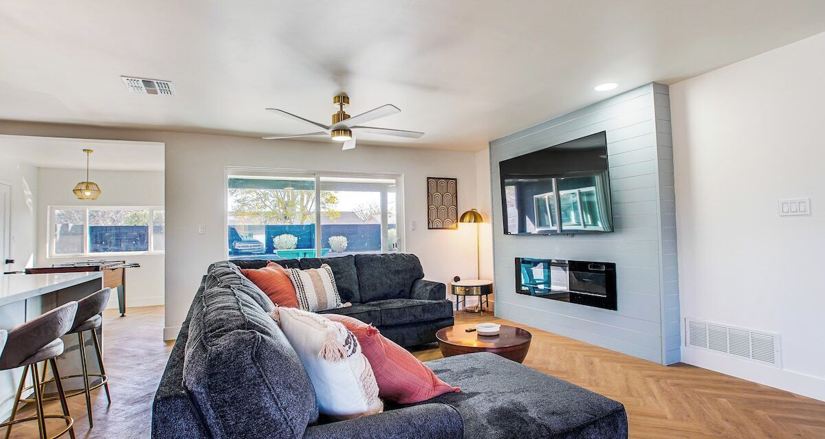A modern living room with a grey sectional sofa, a TV mounted on the wall, and a ceiling fan.