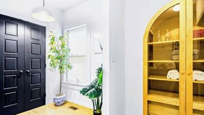 A room with a black door, a window with blinds, a potted plant, a wooden cabinet with shelves, and a light fixture. - Walk to BeltLine, Stylish 2BR w/ Deck, Sleeps 4 (Atlanta)