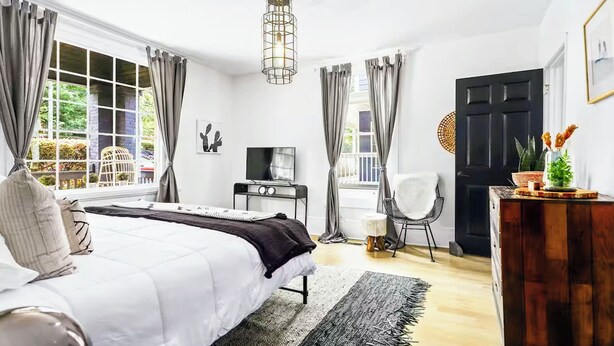 A bedroom with a bed, a desk, a chair, a TV, and a door. - Walk to BeltLine, Stylish 2BR w/ Deck, Sleeps 4 (Atlanta)