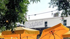 An outdoor seating area with yellow tables and umbrellas, a building with 'Ladybird' signage, and people dining. - Walk to BeltLine, Stylish 2BR w/ Deck, Sleeps 4 (Atlanta)