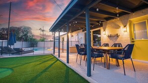 Ein Patio mit Pool, einer überdachten Sitzgruppe mit Tisch und Stühlen und einer gelben Tür.