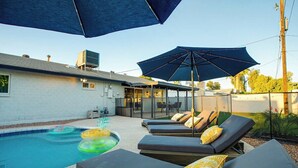 Ein Poolbereich mit Liegestühlen und Sonnenschirmen, ein klarer Himmel und ein Gebäude im Hintergrund.