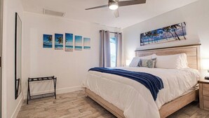 Ein Schlafzimmer mit Bett, Deckenventilator, einem Bild und einem Fenster mit Vorhängen.