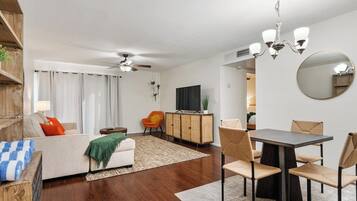 Een moderne woonkamer met een bank, eettafel en stoelen. Achterin staat een televisie en een kast.