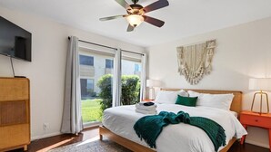 Un dormitorio con cama, ventilador de techo, televisión, mesita de noche y vistas al exterior.