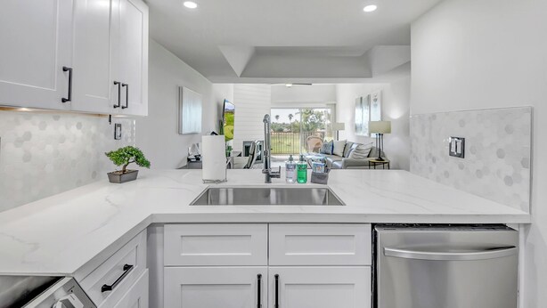 Una cocina moderna con gabinetes blancos, un lavamanos de acero inoxidable y un lavavajillas.