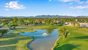 Un campo de golf con un estanque, árboles y una cadena montañosa al fondo.
