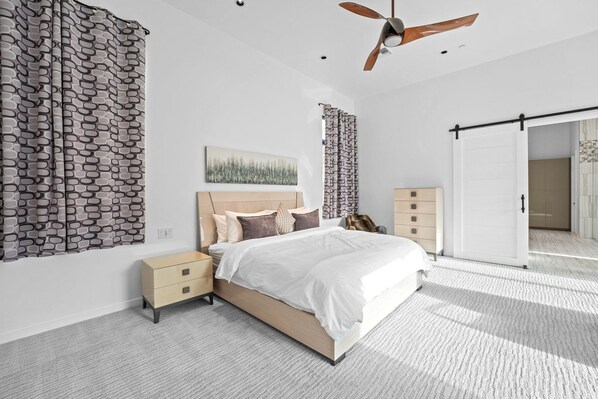 A modern bedroom with a bed, nightstands, a ceiling fan, and a sliding door.