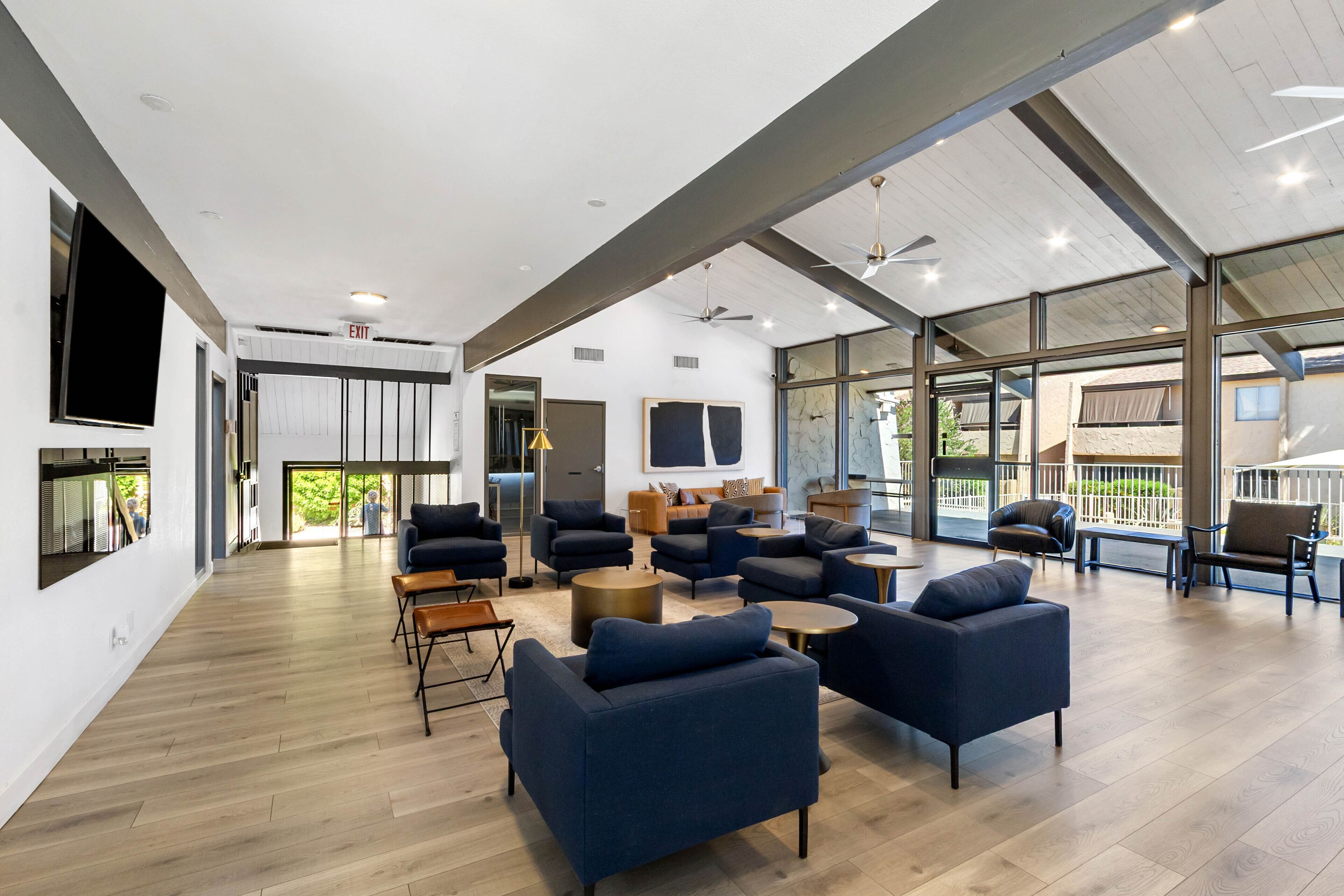 A spacious, modern lounge area with multiple seating options, large windows, and a high ceiling with exposed beams.