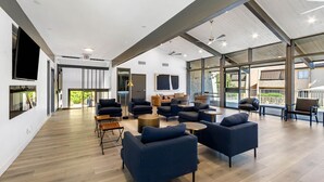 Un espace salon spacieux et moderne, doté de nombreux sièges, de grandes fenêtres et d’un plafond haut avec des poutres apparentes.