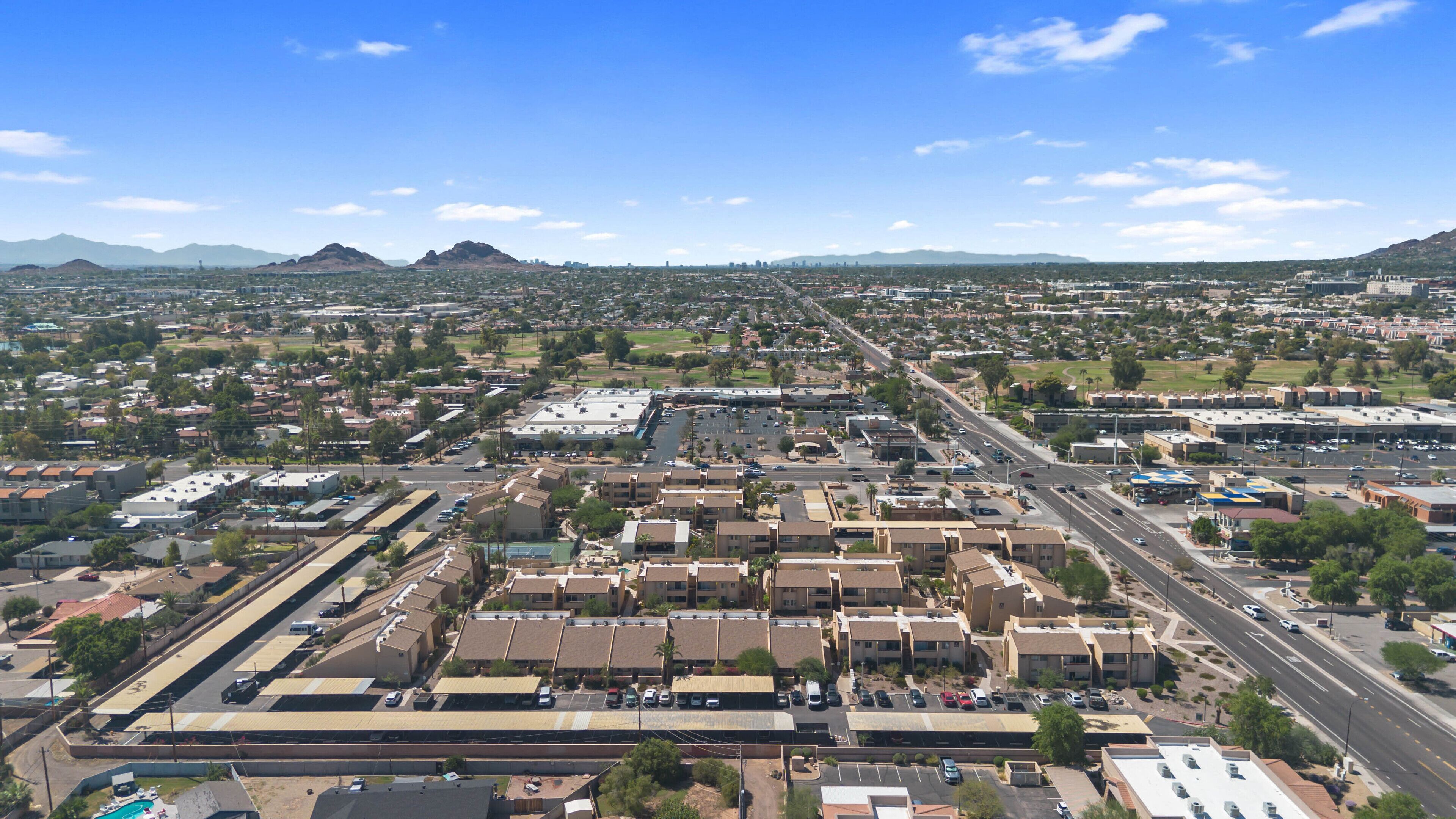 A wide aerial view of a city with a mix of residential and commercial buildings, roads, and distant mountains.