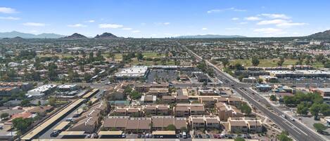 A wide aerial view of a city with a mix of residential and commercial buildings, roads, and distant mountains.