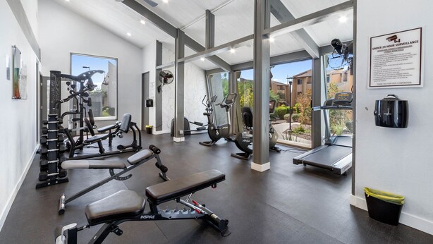 Une salle de sport moderne équipée de divers appareils d’exercice, dotée de grandes fenêtres et d’un ventilateur de plafond.