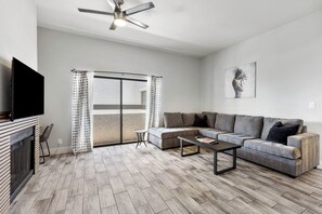 A modern living room with a sofa, coffee table, TV, fireplace, and a ceiling fan.