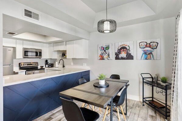 Una cocina moderna con armarios blancos, microondas integrado y un comedor con mesa y sillas de madera.