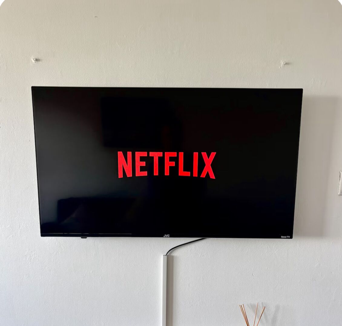 A flat-screen TV mounted on a wall with the Netflix logo displayed on the screen.
