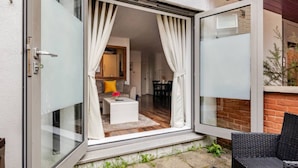 An open sliding glass door leading to a living area with a sofa, coffee table, and curtains. - Canary Wharf Gem - Prvt Parking - Fast WiFi - O2 & Excel - Sleeps 4 (London)