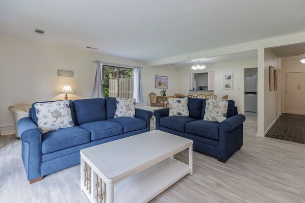 A living room with two blue sofas, a white coffee table, and a dining area with a table and chairs. - Updated Family Villa | Patio, Walk to Pool/Beach/Trails/Tennis, Bikes (Hilton Head Island)