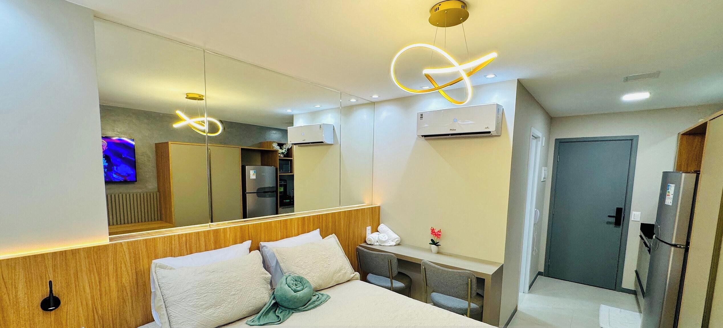 A hotel room with a bed, bedside table, mirror, air conditioning unit, and a door.
