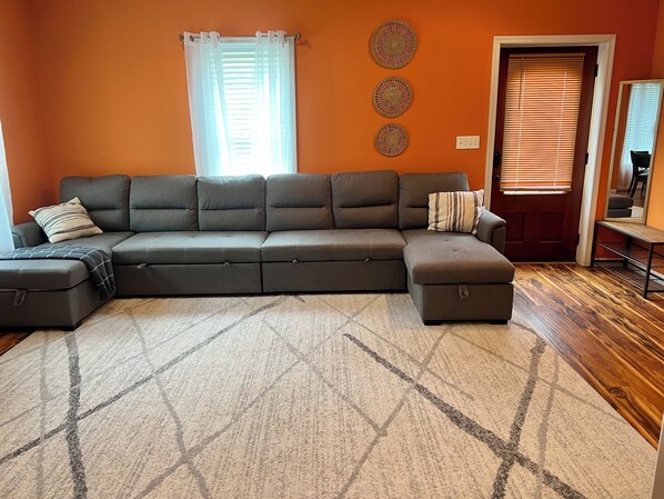 A sectional sofa with storage ottoman, a patterned rug, and decorative wall art. - Charming 1-bedroom bungalow in lovely Roebuck (Roebuck)