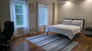 Un dormitorio con cama, una silla y ventana.