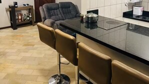 A modern kitchen with a black countertop, white cabinets, and a built-in oven. There are three bar stools and a dark-colored chair. - The most complete and in the best location in Florianópolis-SC. (florianópolis)