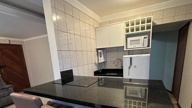 A modern kitchen with a black countertop, white cabinets, a microwave, and a built-in oven. There are three bar stools with metal bases. - The most complete and in the best location in Florianópolis-SC. (florianópolis)