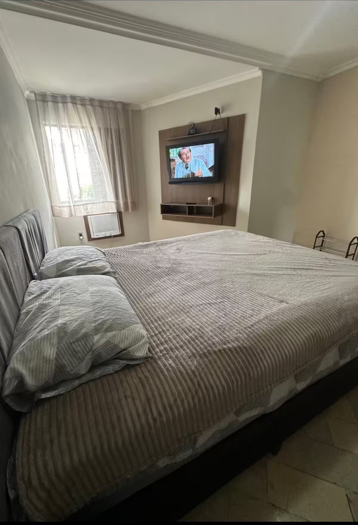 A hotel room with a large bed, a television mounted on the wall, and a window with curtains.