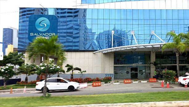 A modern hotel with a large glass facade and a prominent logo. - Dolphins Tech (Salvador)