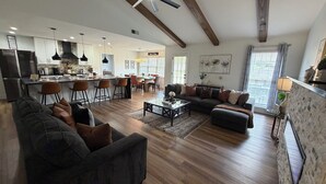 En rummelig stue med en stor sofa, et sofabord og et spiseområde med stole samt et køkken i baggrunden.