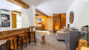 Eine moderne Küche mit Holzelementen, ein Essbereich mit Hockern, eine gemütliche Sitzecke und eine Treppe, die zu einer oberen Ebene führt.