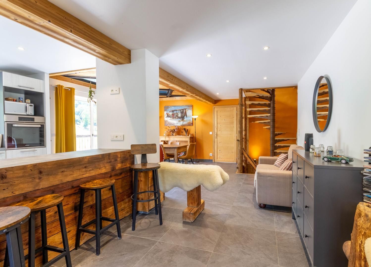 Een moderne keuken met houten details, een eethoek met krukken, een gezellige zithoek en een trap naar een verdieping erboven.