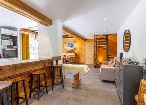 Een moderne keuken met houten details, een eethoek met krukken, een gezellige zithoek en een trap naar een verdieping erboven.