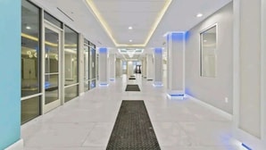 A modern, well-lit hallway with glass doors on the left, leading to rooms. - Spectacular views - direct oceanfront studio w/kitchen & pool (Daytona Beach)