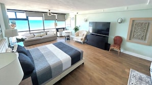 A spacious living room with a large bed, a TV, and a view of the ocean. - Spectacular views - direct oceanfront studio w/kitchen & pool (Daytona Beach)