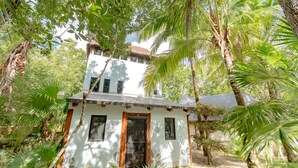 A small white building with a thatched roof, surrounded by lush greenery and palm trees.