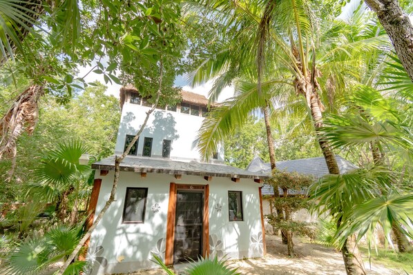 A small white building with a thatched roof, surrounded by lush greenery and palm trees.