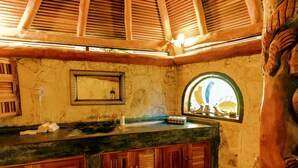 A rustic bathroom with a stone wall, wooden cabinets, a sink, and a window with a view.