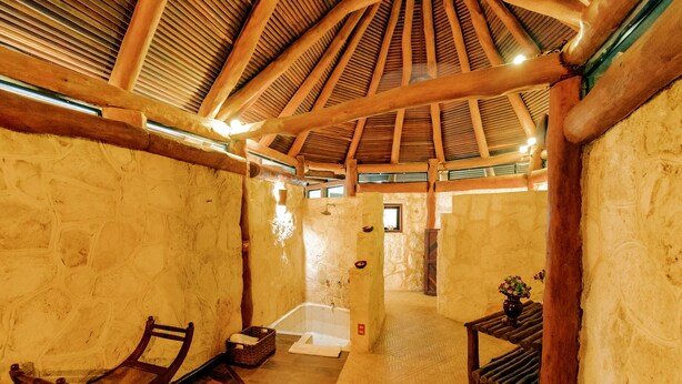 A rustic interior with a stone wall, wooden beams, a bathtub, and a wooden bench.