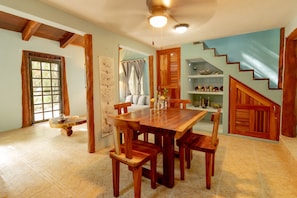 A dining area with a wooden table and chairs, a ceiling fan, and a staircase with a wooden railing.