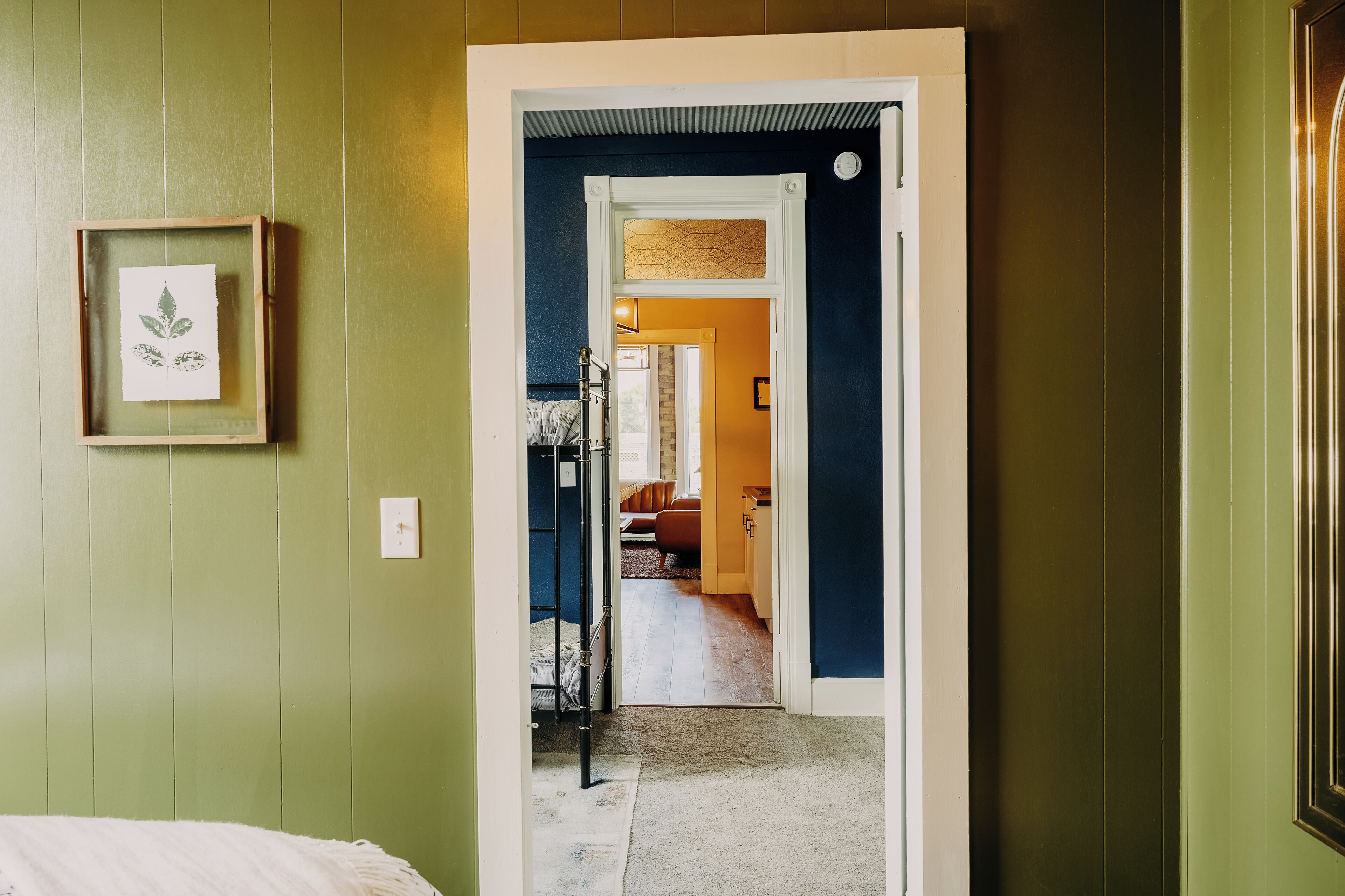 A hallway with a bed on the left, a door leading to another room, and a framed picture on the wall.