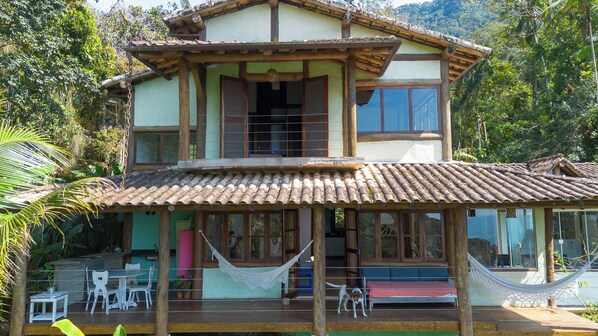 A two-story house with a wooden deck, a hammock, and a dining area with chairs and a table.