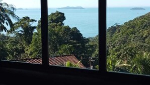 A view through a window of a coastal landscape with a clear sky, lush greenery, and distant islands. - Felix Ocean View, Ubatuba, Sao Paulo, Brazil. (Ubatuba)